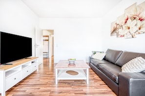 Ein modernes Wohnzimmer mit Flachbildfernseher, Couchtisch, Sofa und einem Gemälde an der Wand.