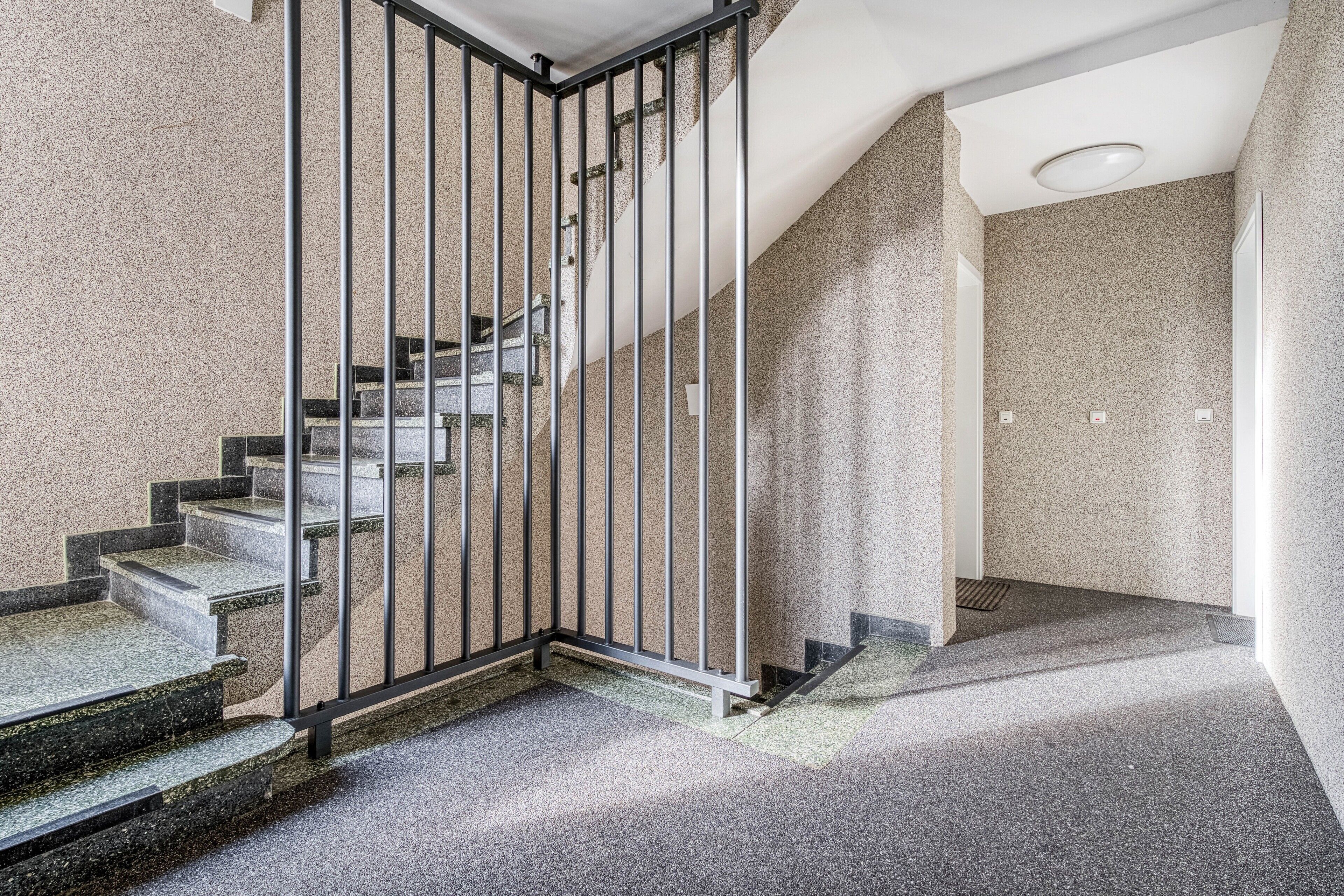 Una escalera con barandillas de metal, peldaños alfombrados y una pared texturizada.