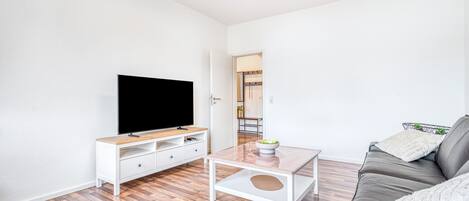 A modern living room with a flat-screen TV, a white coffee table, a leather sofa, and a wooden floor.