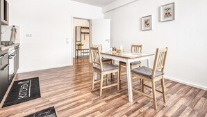 Una cocina moderna con encimera de madera, un comedor con mesa blanca y sillas de madera, y un pasillo que conduce a otra habitación.