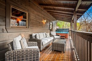 A wooden deck with wicker furniture, a hot tub, and a large window overlooking a natural landscape. - 1/2 Mile Parkway*2BR*Hot Tub*Games*Families*Pools (Pigeon Forge)