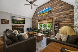 Ein Wohnzimmer mit Kamin, Ledersofas, einem Couchtisch und einem großen Fenster mit Blick auf Grünflächen.