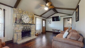 A living room with a stone fireplace, wooden flooring, a ceiling fan, a television, and a sofa. - Turner Escape Cabins #3 (Davis)