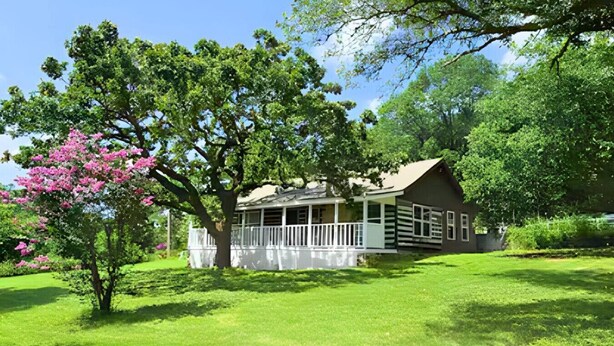 A two-story house with a porch, surrounded by lush green grass and trees. - Turner Escape Cabins #3 (Davis)