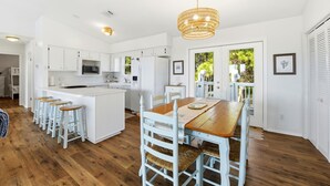A modern kitchen with white cabinetry, a wooden dining table, and a hanging light fixture. - WELCOME TO DOC'S HOLIDAY! (St. George Island)