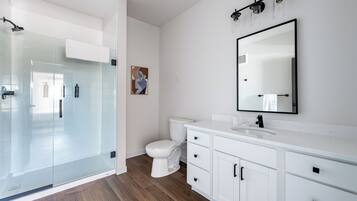 A modern bathroom with a glass shower enclosure, a white toilet, and a white vanity with a large mirror.