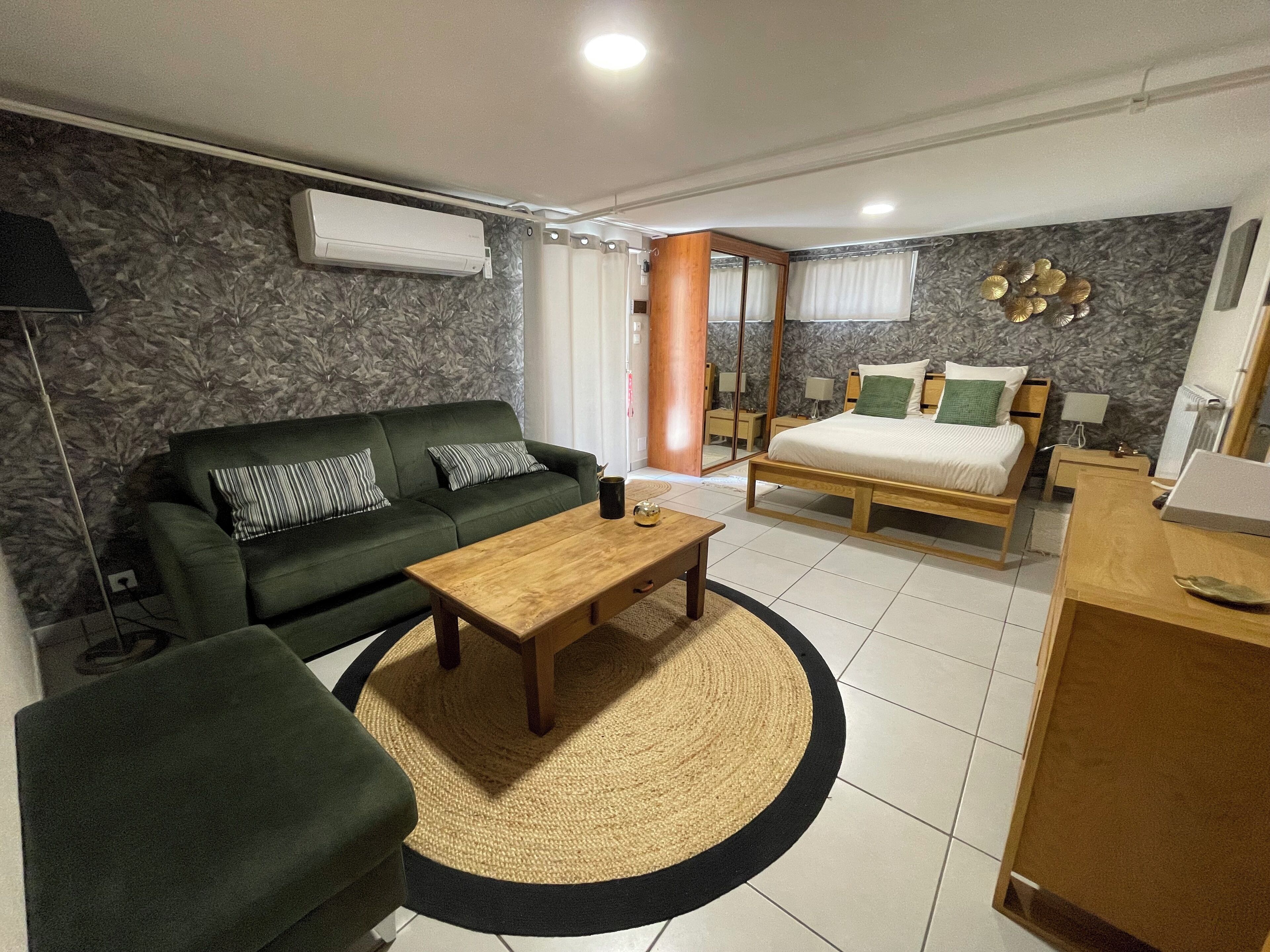 Une chambre d’hôtel moderne avec un canapé vert, un lit en bois, une petite table en bois et un tapis rond.