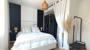 A modern bedroom with a large bed, a bedside table, a lamp, a glass shower enclosure, and a standing mirror. - A stone's throw from the medieval town, pretty house ideal for families (Carcassonne)