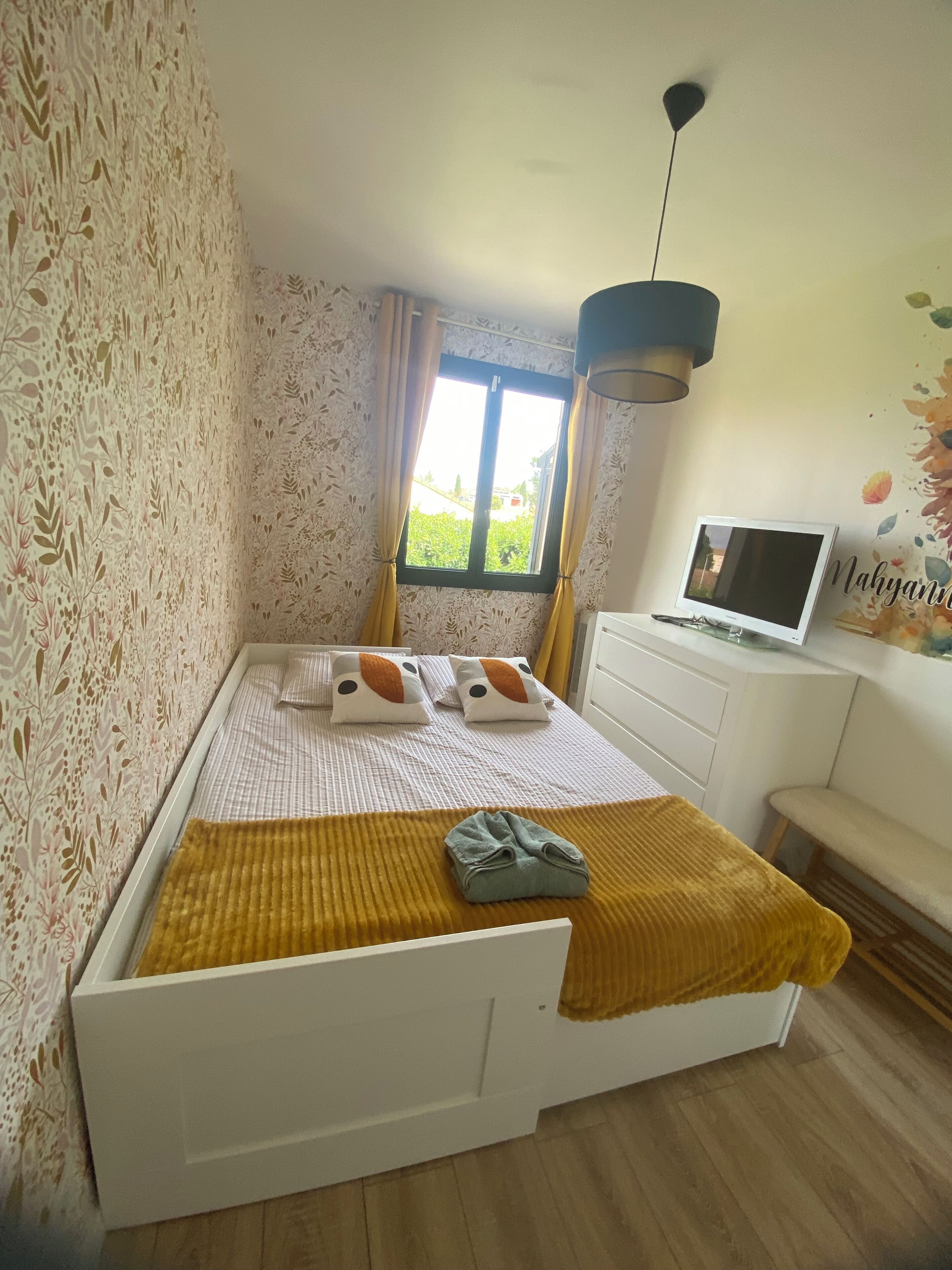 Una camera da letto con un letto, una TV, una scrivania e una finestra con tende.