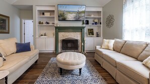 Una sala de estar con chimenea, sofás, televisor y objetos decorativos en estantes.