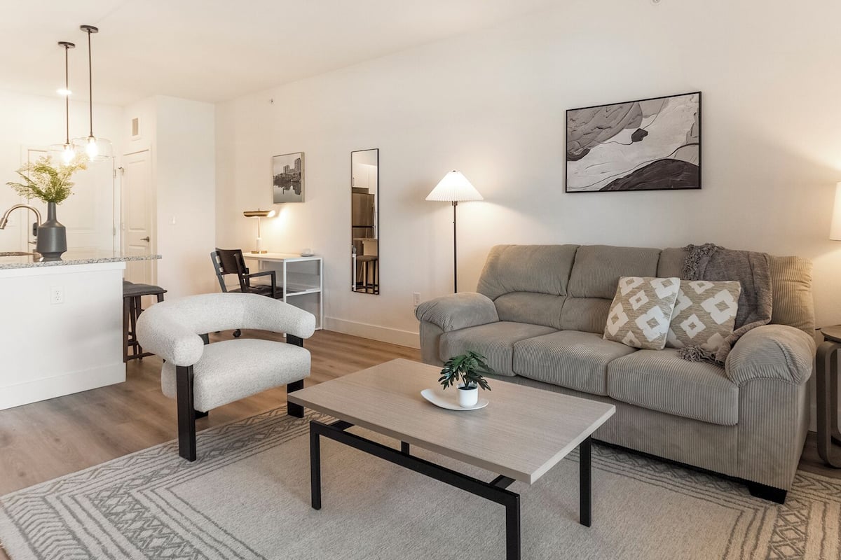A modern living room with a sofa, a coffee table, and a dining area with a chair and a small table.