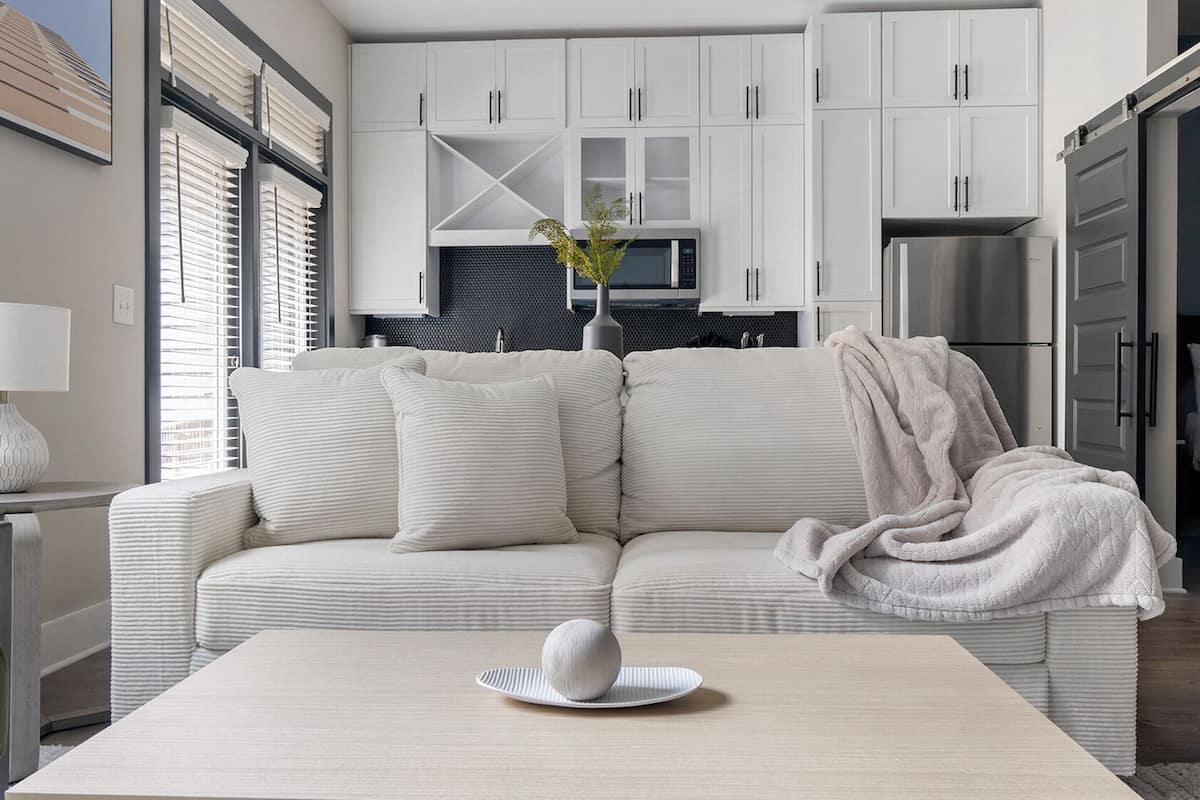 A modern living room with a sofa, a coffee table, and a kitchen area in the background.
