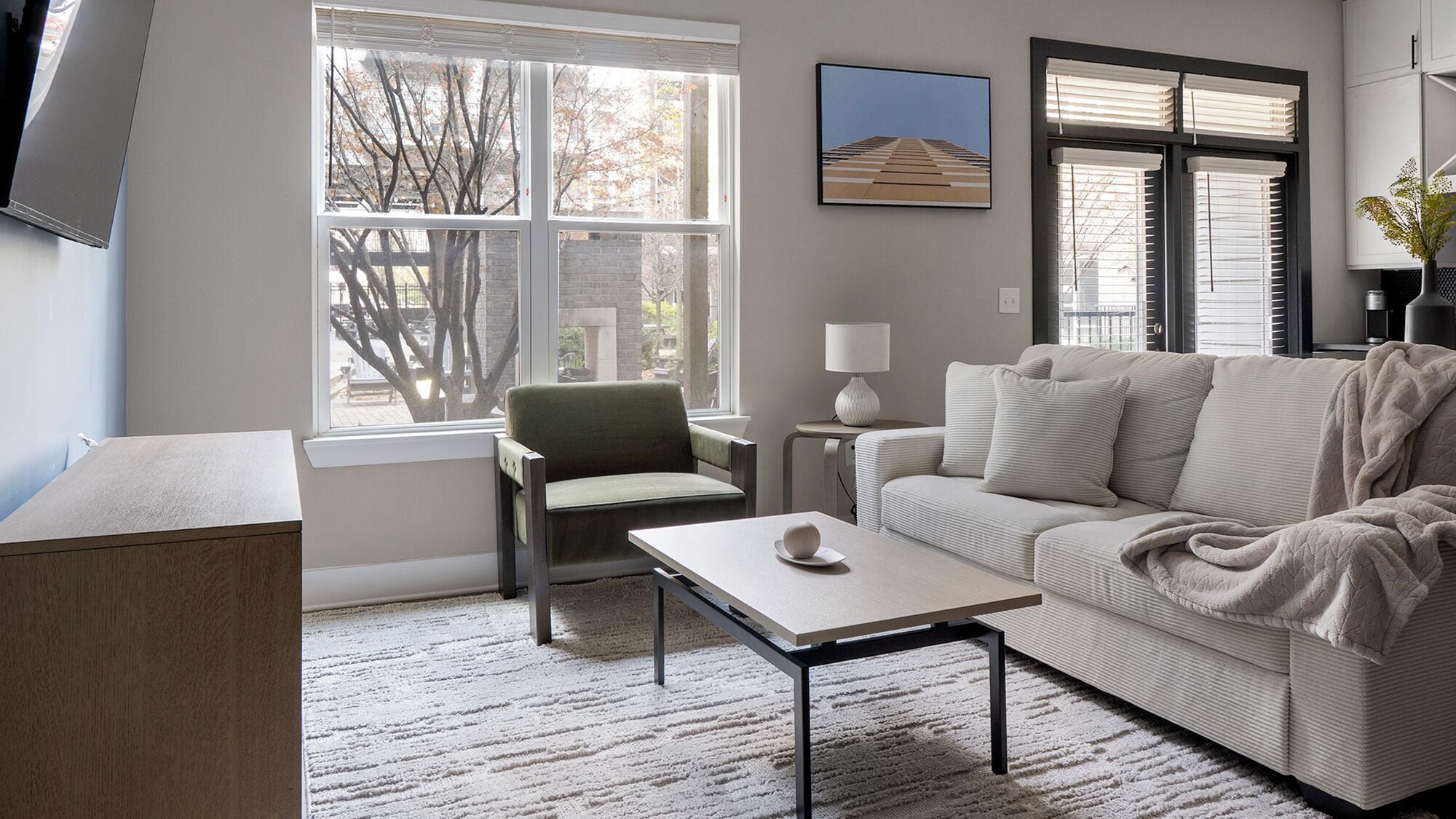A modern living room with a sofa, a chair, a coffee table, and a TV mounted on the wall.