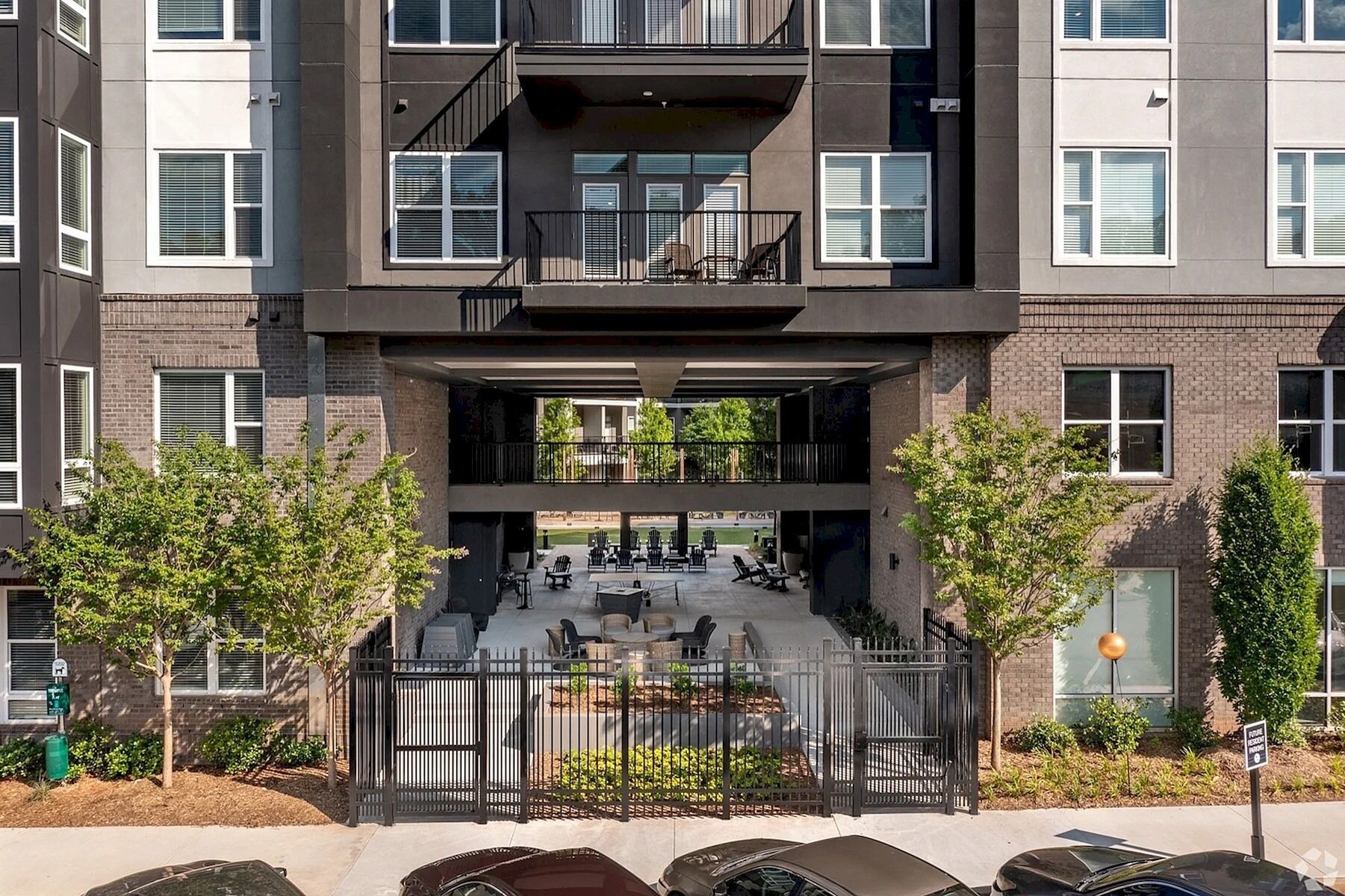 A multi-story building with a covered outdoor seating area, a gated entrance, and a mix of brick and concrete exterior.