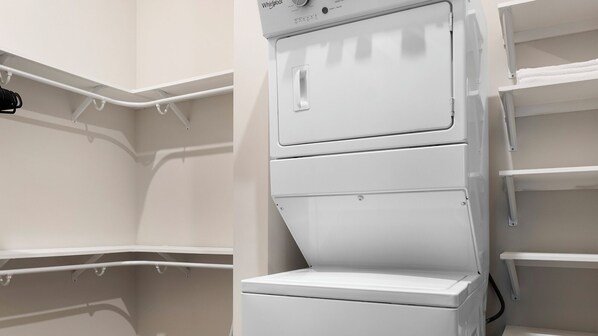A white Whirlpool washer and dryer unit with a control panel, installed in a corner of a room with white walls and shelving units.
