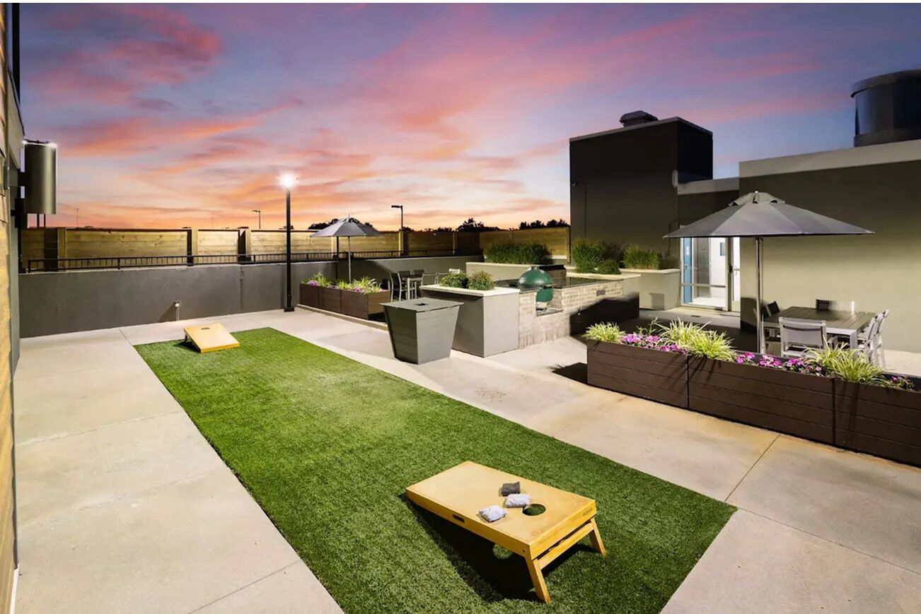 A rooftop patio with a green lawn, outdoor seating, and a barbecue area.
