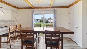 A dining area with a wooden table and chairs, a chandelier, and a view through a glass door. - Large family friendly country home (Monett)