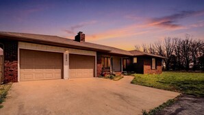 A two-story house with a garage, brick exterior, and a driveway leading to the front door. - Large family friendly country home (Monett)
