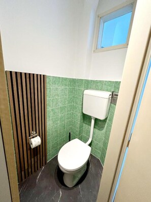 A small, compact bathroom with a toilet, green tiles, and a window. - 2 rooms apartment near Schönbrunn palace (Vienna)