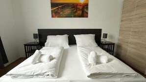 A double bed with white linens and pillows, a nightstand with a lamp, and a painting of a sunset on the wall. - 2 rooms apartment near Schönbrunn palace (Vienna)