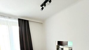 A modern dining area with a wooden table, four grey chairs, a small potted plant, and a built-in TV shelf. - 2 rooms apartment near Schönbrunn palace (Vienna)
