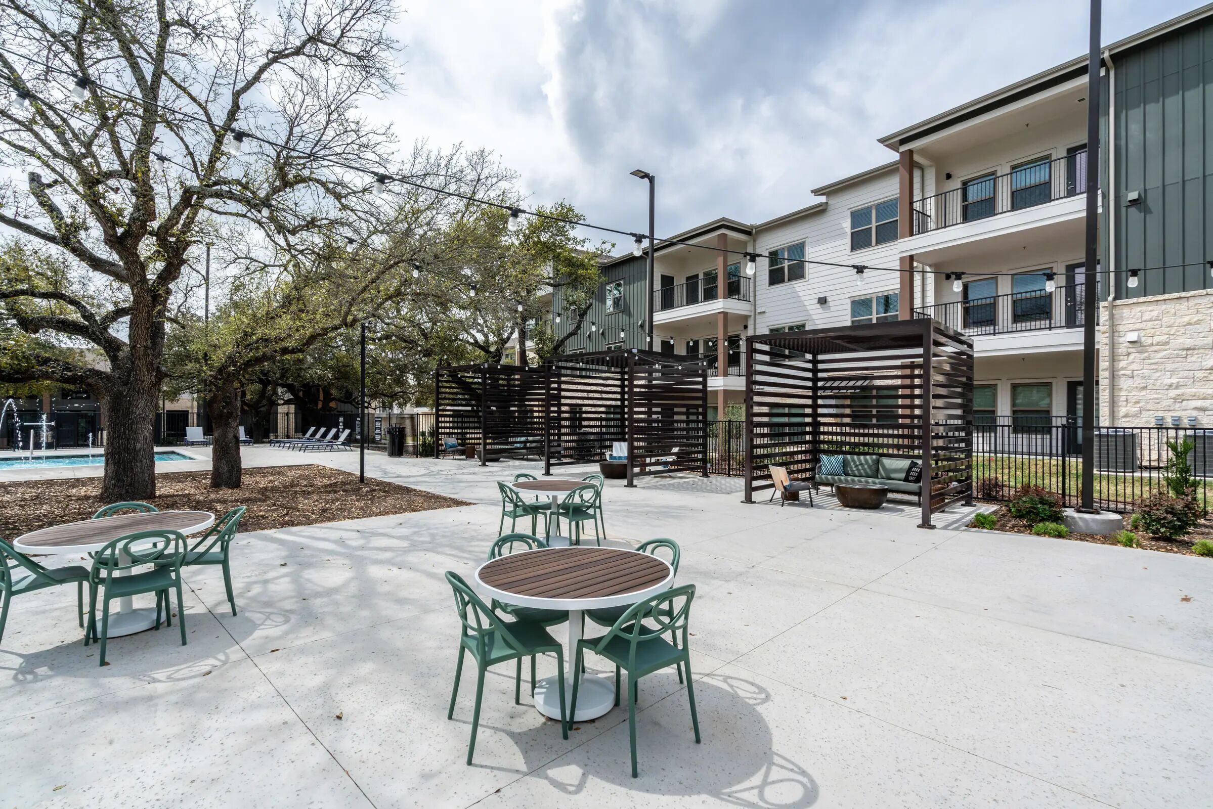 Un patio con mobiliario exterior, piscina y un edificio con balcones.