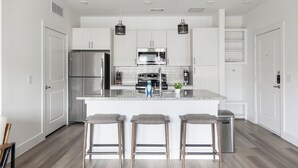 A modern kitchen with white cabinetry, stainless steel appliances, a granite countertop, and three bar stools. - Landing Apartments - Leander (Leander)