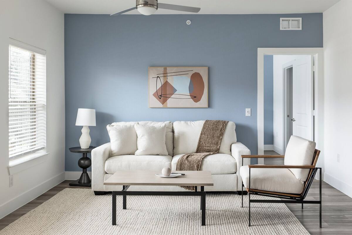 Un salon avec un canapé, une table basse et un fauteuil, un tableau au mur et un ventilateur de plafond.