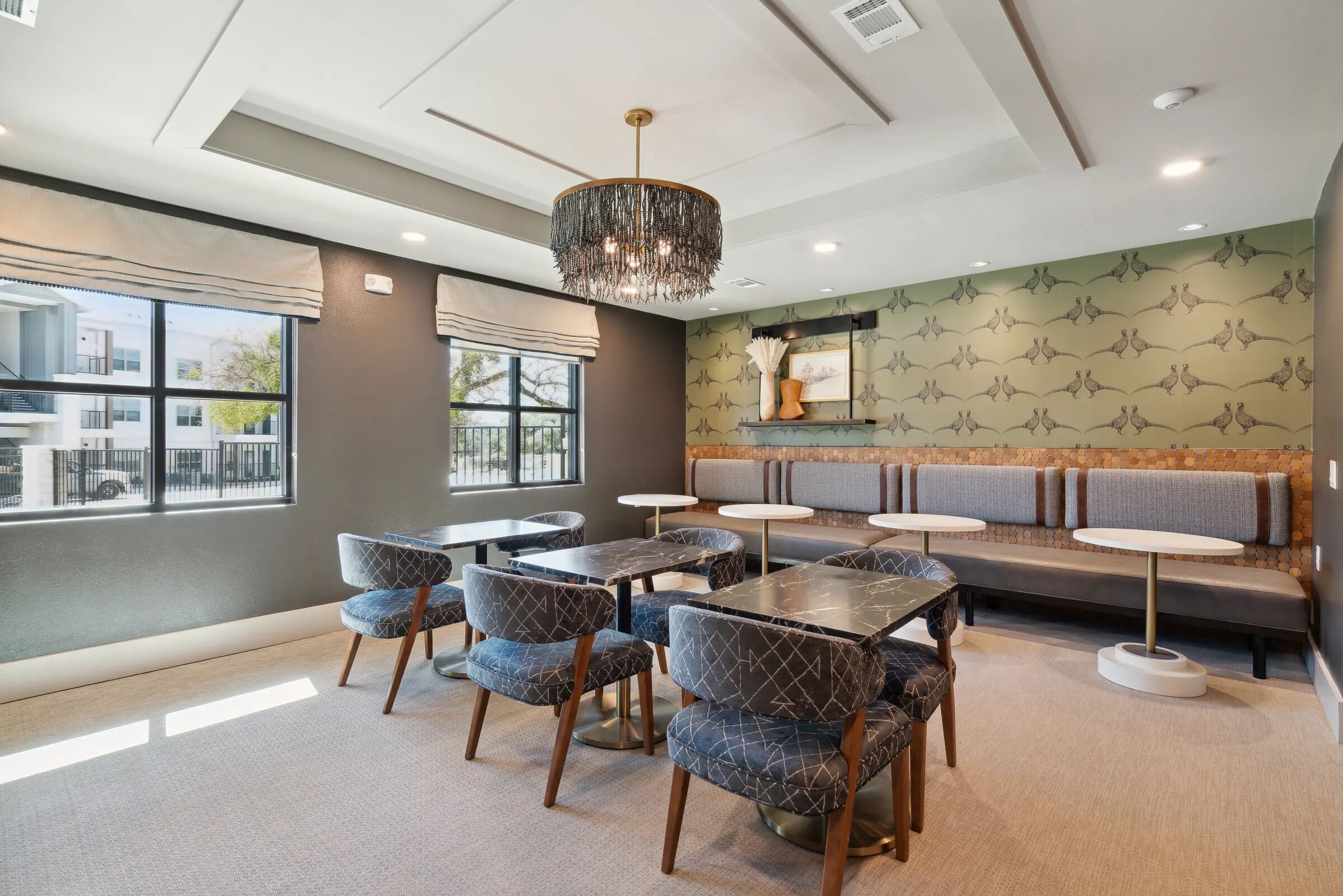 A modern dining area with tables and chairs, a chandelier, and a patterned wall.
