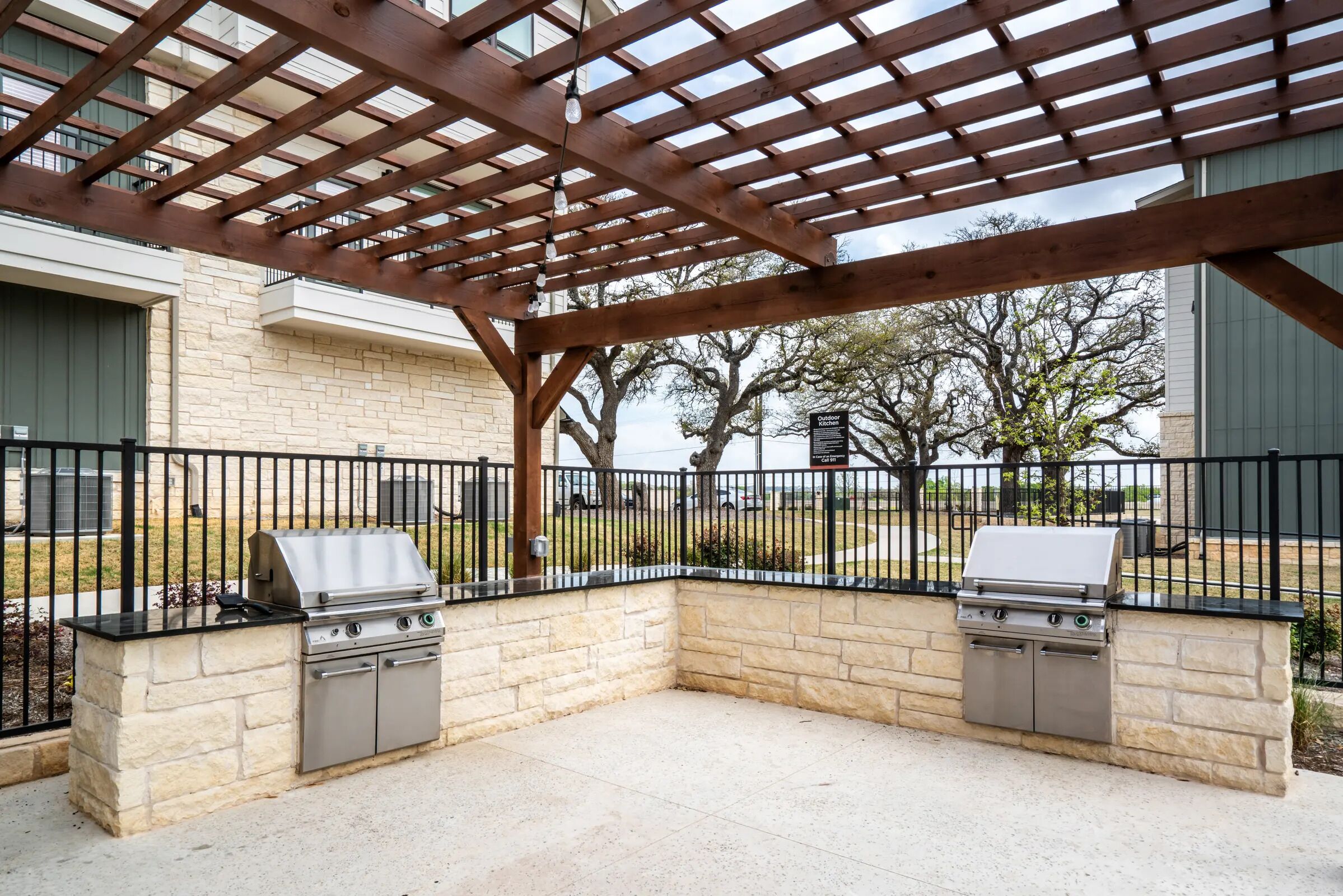 Un patio al aire libre con dos parrillas de barbacoa, una pérgola arriba y un muro de piedra.