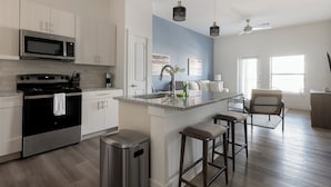 A modern kitchen with white cabinets, stainless steel appliances, a granite countertop, and a bar stool seating area. - Landing Apartments - Leander (Leander)