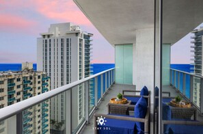 Un balcón con mobiliario de mimbre, vista al océano y edificios altos al fondo.