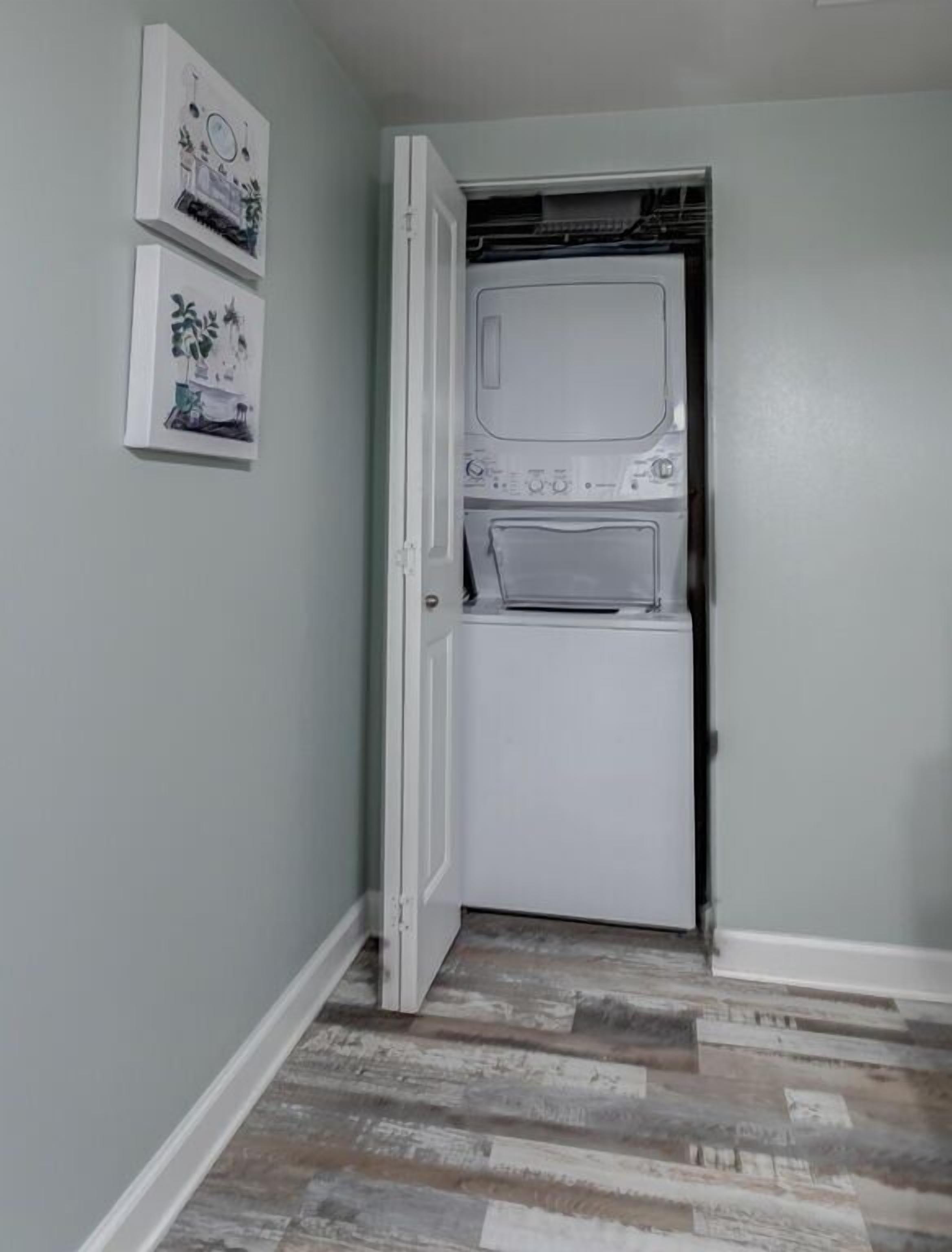 A laundry room with a dryer and a washing machine, a wooden floor, and two framed pictures on the wall.