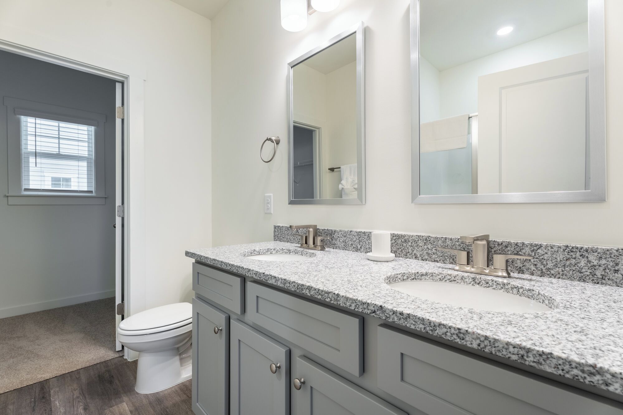 A bathroom with a white toilet, granite countertops, a large mirror, and a towel rack.