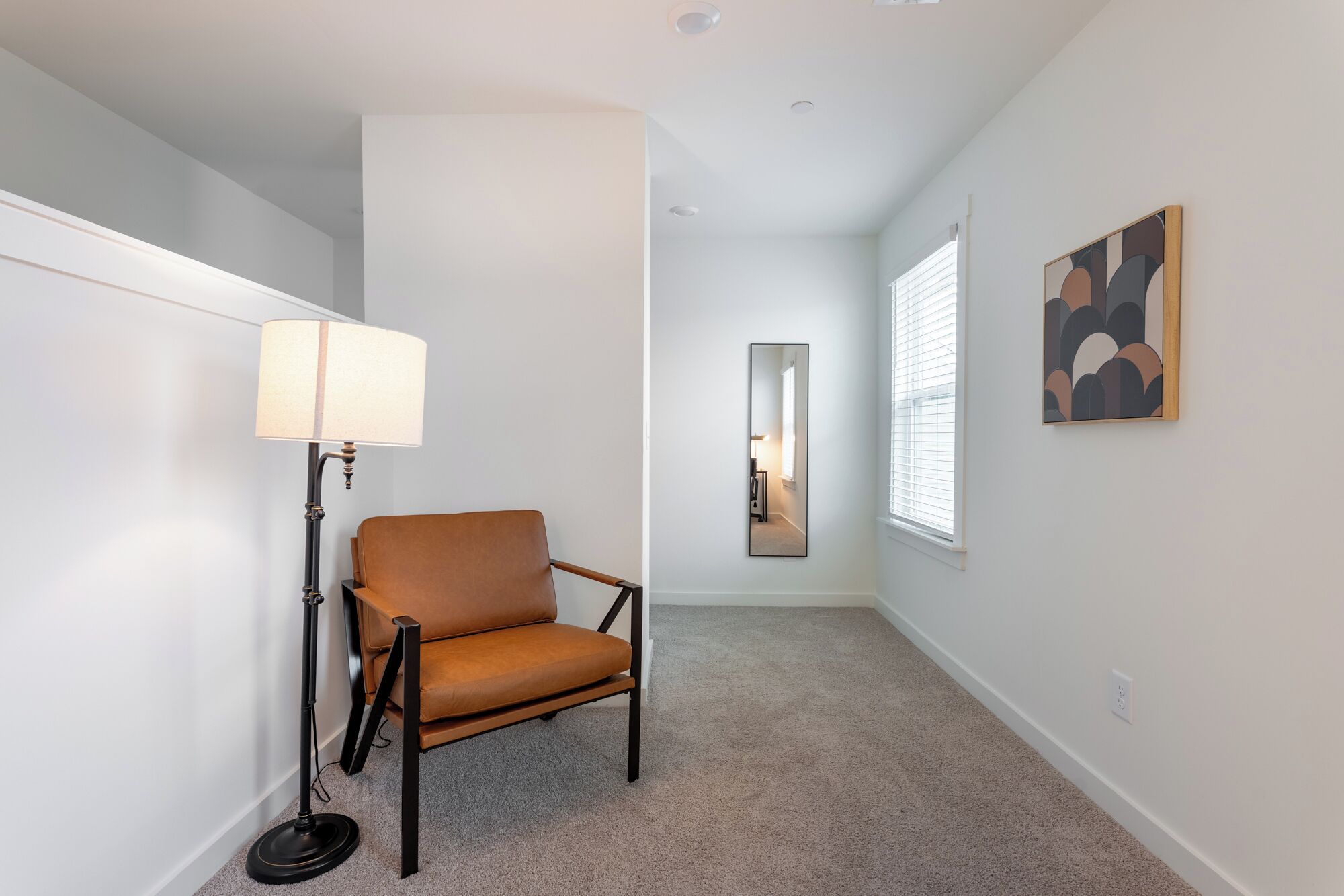 A hallway with a brown leather chair, a floor lamp, and a mirror on the wall.