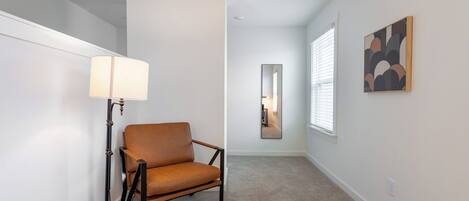 A hallway with a brown leather chair, a floor lamp, and a mirror on the wall.