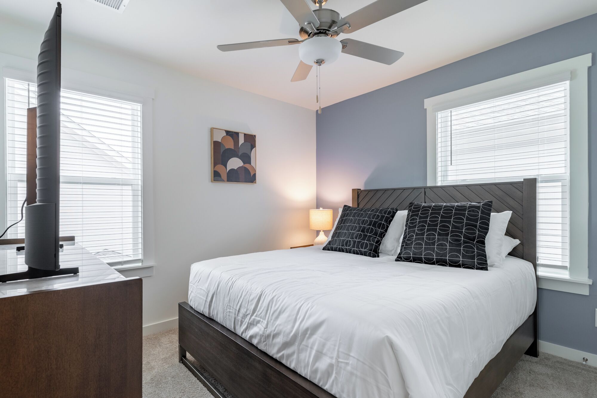 A bedroom with a bed, a ceiling fan, a bedside table, and a lamp.