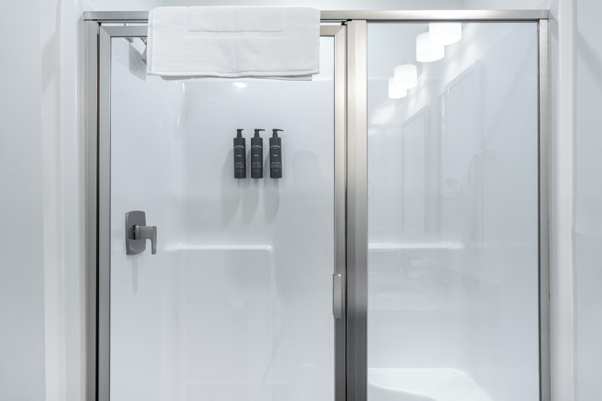 Ein modernes Badezimmer mit Duschabtrennung aus Glas, einem Handtuch an der Tür und zwei Shampoo-Flaschen.