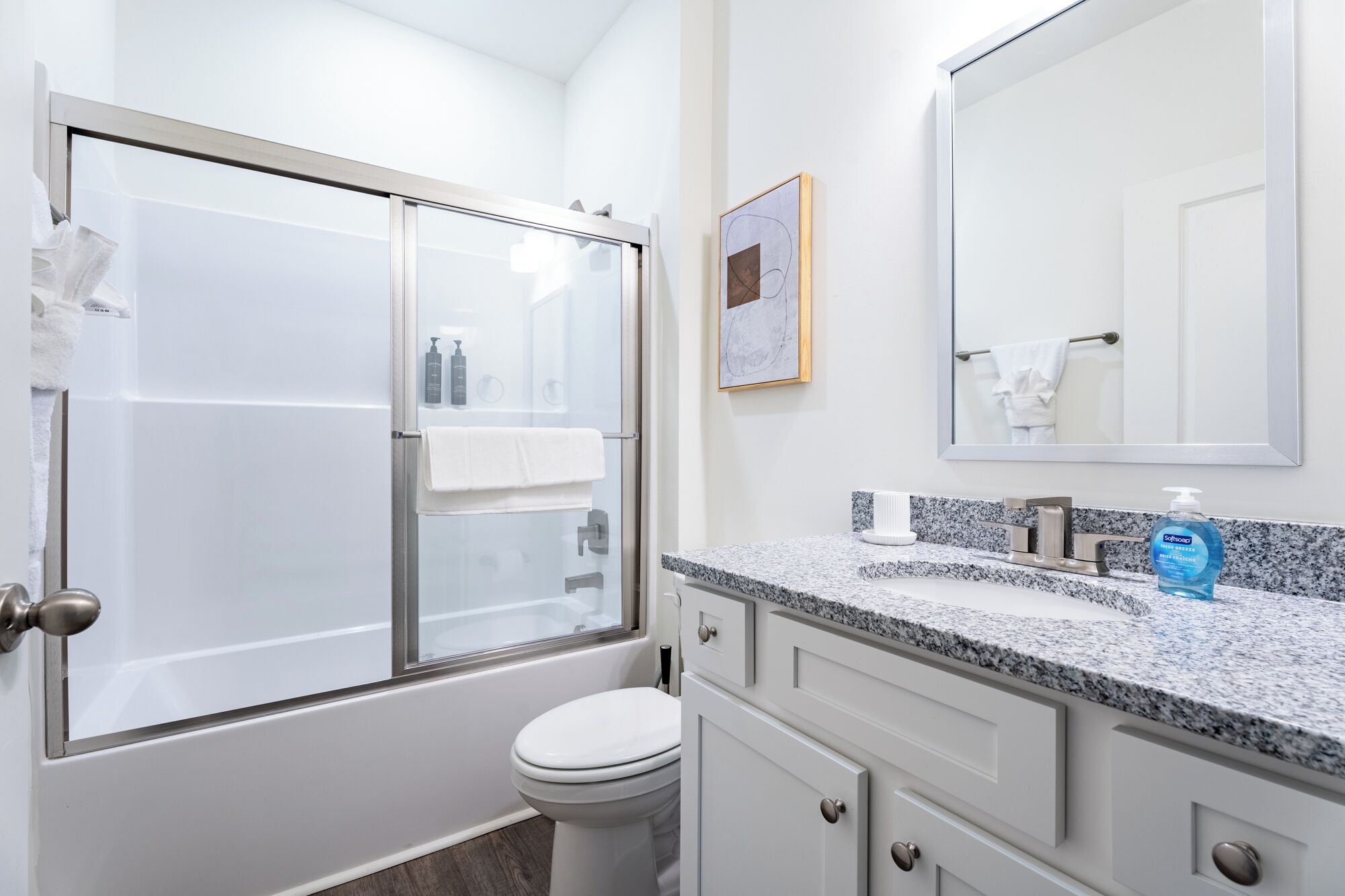 Een badkamer met een douchecabine van glas, een wit toilet, een granieten aanrecht met een wastafel, en een spiegel boven de wastafel.