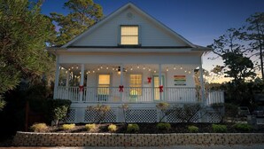 A white two-story house with a porch decorated with string lights and red bows. - Sandy Toes Hideaway 3 Bedroom Home (Tybee Island)