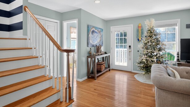 A staircase with wooden steps and white railings, a living room with a Christmas tree, a sofa, and a painting on the wall. - Sandy Toes Hideaway 3 Bedroom Home (Tybee Island)