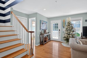 A staircase with wooden steps and white railings, a living room with a Christmas tree, a sofa, and a painting on the wall. - Sandy Toes Hideaway 3 Bedroom Home (Tybee Island)