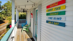 A porch with colorful signs reading "WELCOME," "SANDY TOES," "HIDEAWAY," "TYREEE ISLAND," and "SUN N SURF." - Sandy Toes Hideaway 3 Bedroom Home (Tybee Island)