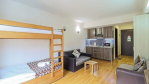 A room with a bunk bed, a sofa, a small table, and a kitchenette area. - New Gudauri Redco Apt. | Comfort by Wehost (Gudauri)
