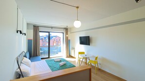 Et hotelværelse med seng, fjernsyn, et vindue med gardiner, et lille bord og en stol.