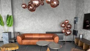 Een moderne woonkamer met een leren bank, een salontafel en een stoel. Sierlijke koperen bollen hangen aan het plafond.