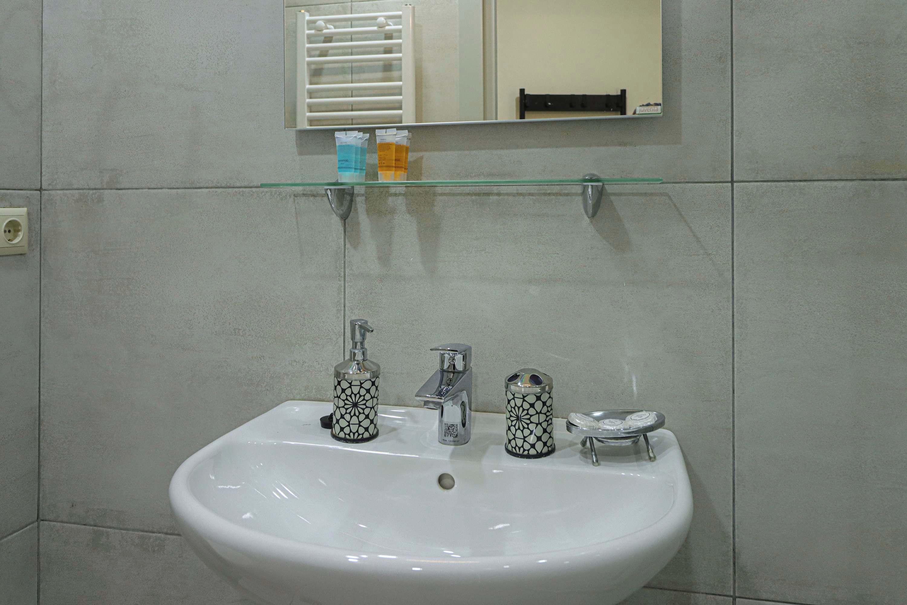 Une salle de bain avec un lavabo blanc, deux distributeurs de savon à motifs et une étagère en verre au-dessus du lavabo.