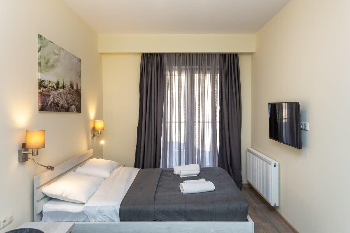 Une chambre d’hôtel avec un lit, deux lampes fixées au mur, un tableau, une télévision et une fenêtre avec des rideaux.
