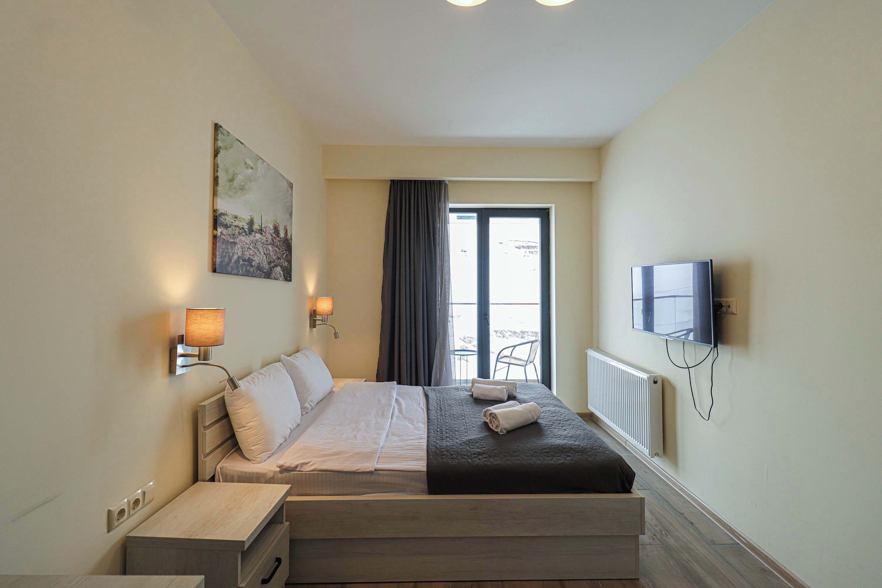 Ein Hotelzimmer mit Bett, Nachttischen, Fernseher und einem Fenster mit Vorhängen.