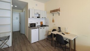 Una cucina compatta con forno a microonde, tostapane e piccolo frigorifero. C'è un tavolo da pranzo con sedie e una lampada a sospensione.